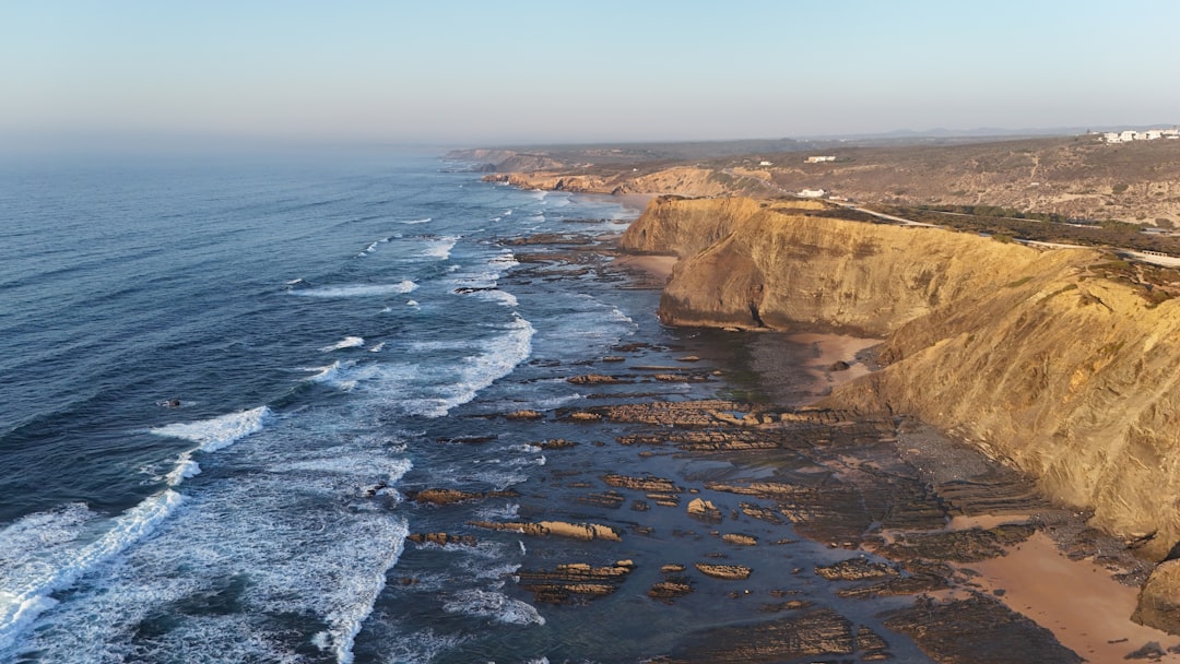 A travel creator filming a stunning coastal landscape at golden hour with a mirrorless camera